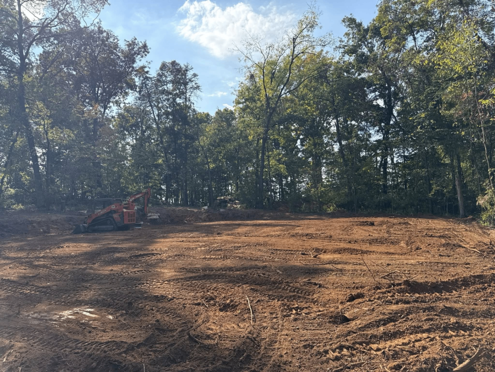 Freshly cleared and graded wooded lot with skid steer ready for building