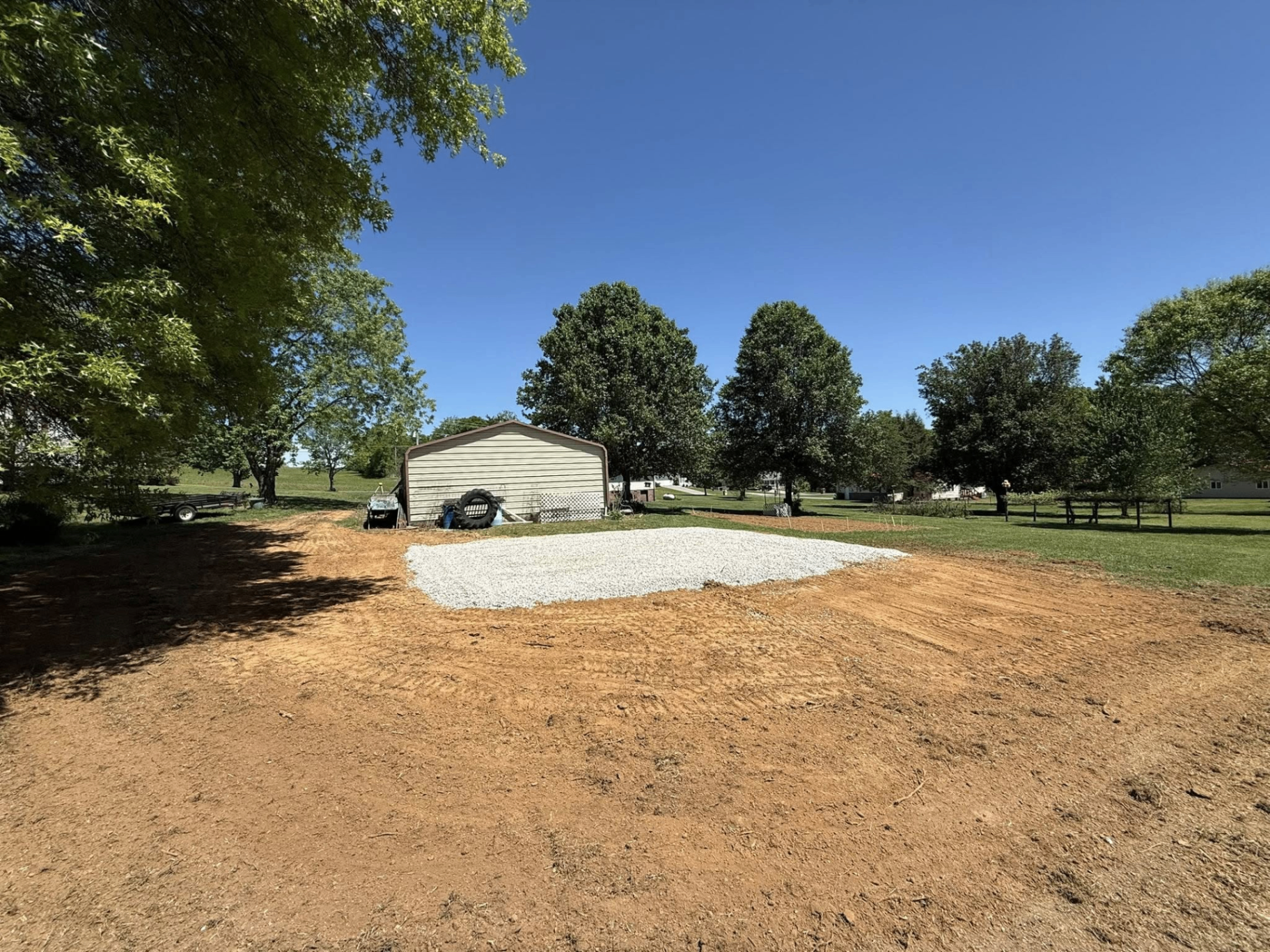 Graded lot with new gravel pad poured in front of a metal garage