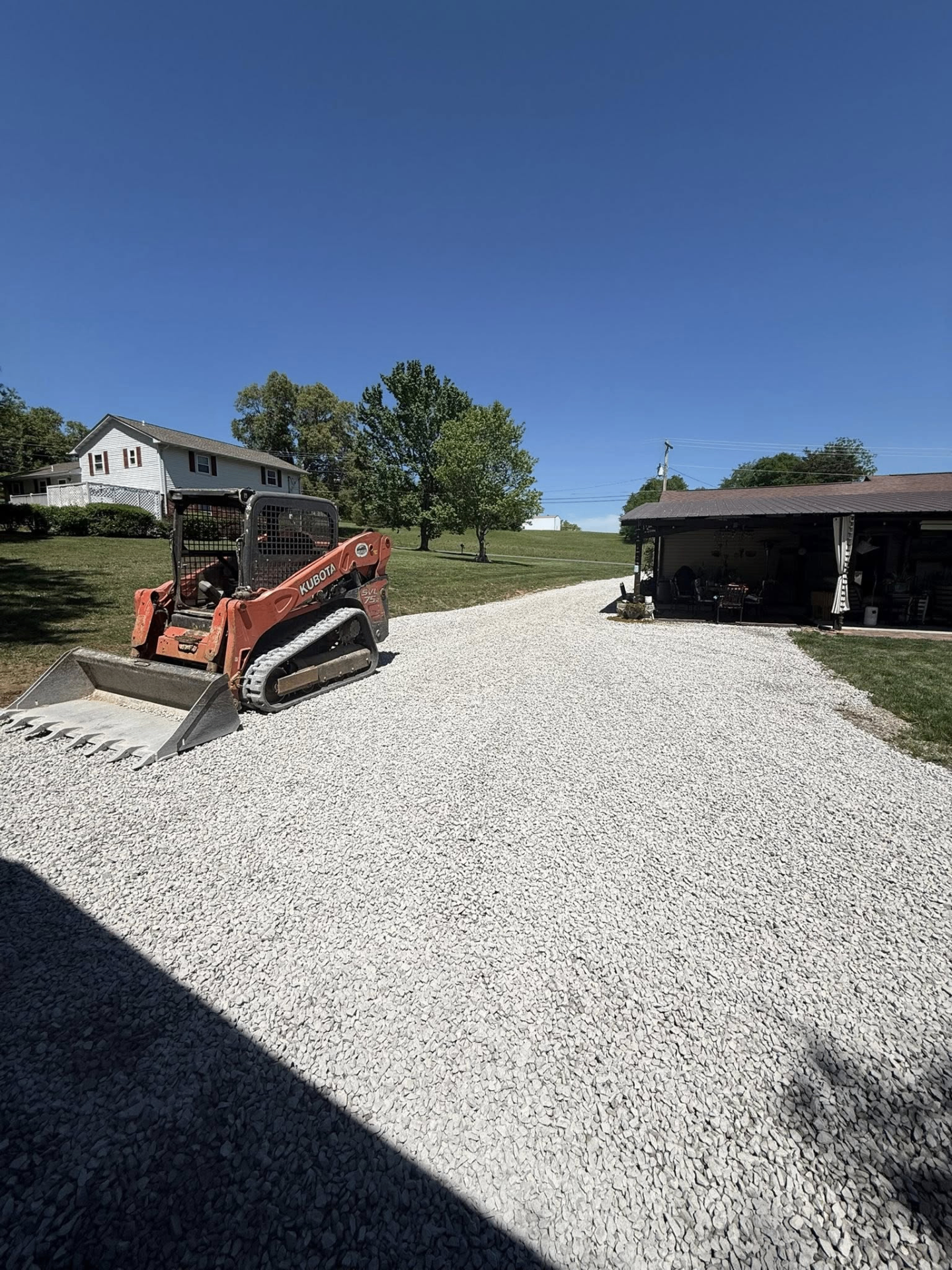 Fresh gravel driveway laid up to a residential carport with skid steer