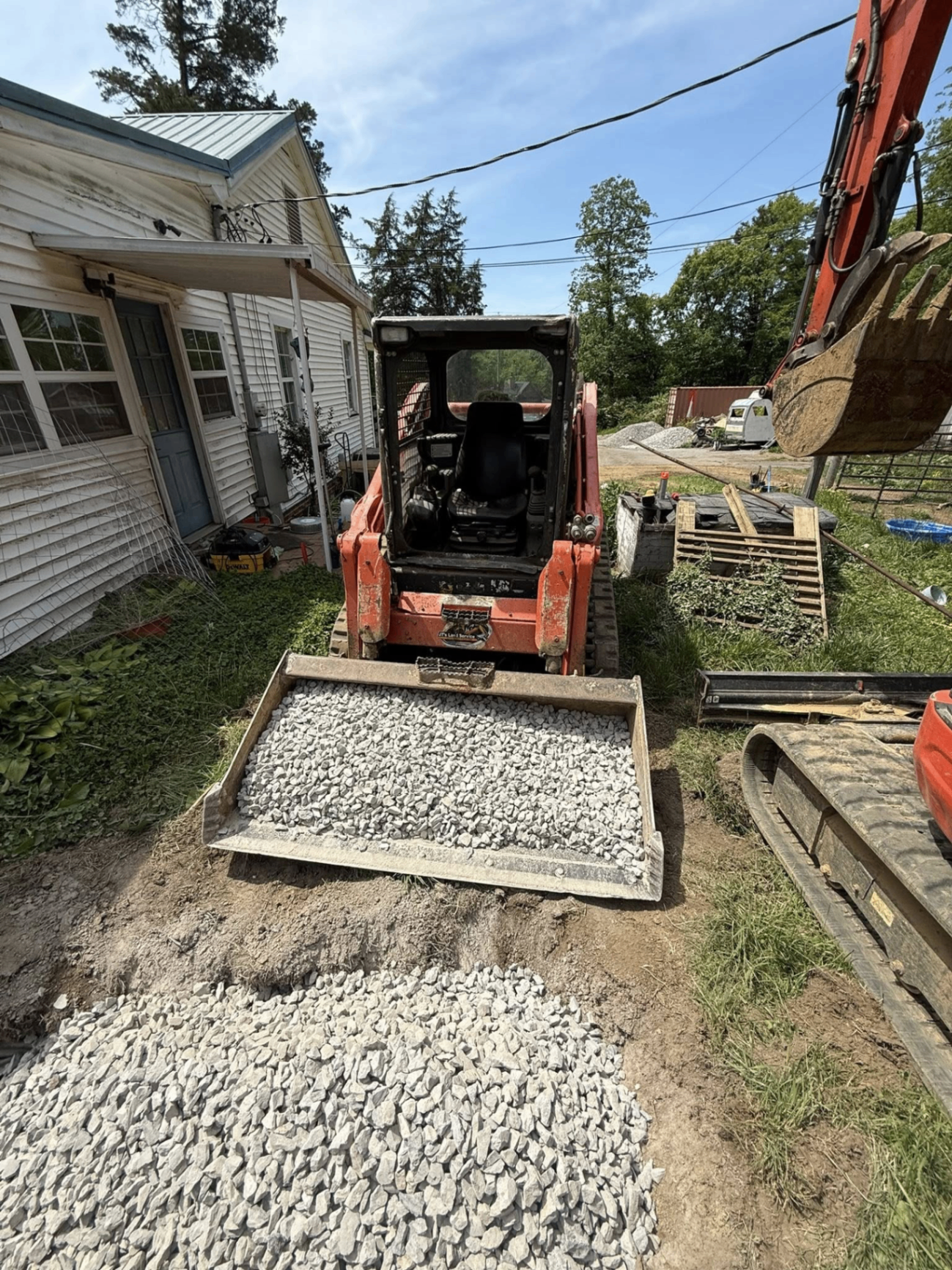 Skid steer spreading gravel for a side-yard pad next to a home