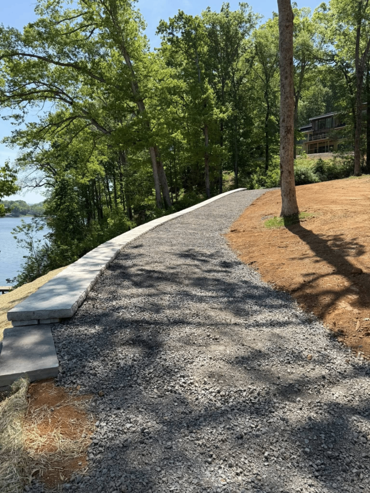 Curved lakeside gravel walkway with stone border on a wooded lot